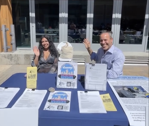 Natalia and JCFC rep sit at a table outside the SSU Rec center and are waving at the camera