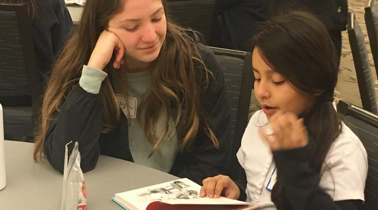 An SSU student and a young student reading and enjoying a snack to start off the day