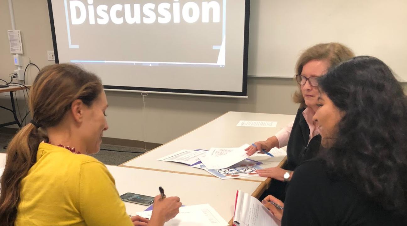 Three participants talking at their tables in front of the projector
