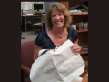 Carolyn Warren sits smiling in a chair in the CCE. She is holding a canvas bag in front of her.