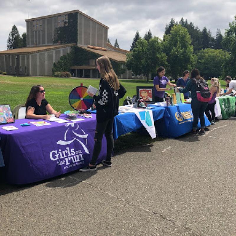 A row of tables with posters outside and people attending them