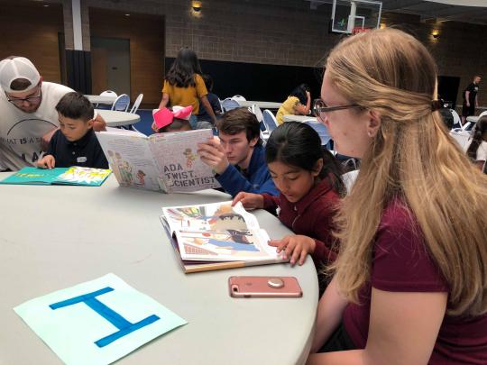 Elementary school students read to college students around a table