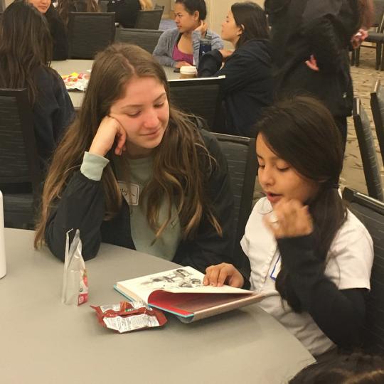 An SSU student and a young student reading and enjoying a snack to start off the day