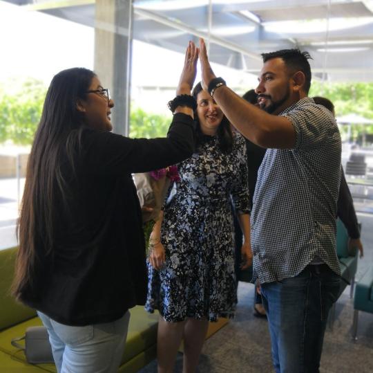 Pam Rivas & her supervisor, Eliot Enriquez high five as Merith Weisman, Director of the CCE looks on.