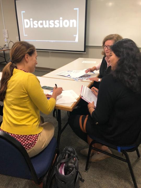 Three participants talking at their tables in front of the projector