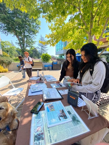 Two students stand at the a table outside looking at resource materials