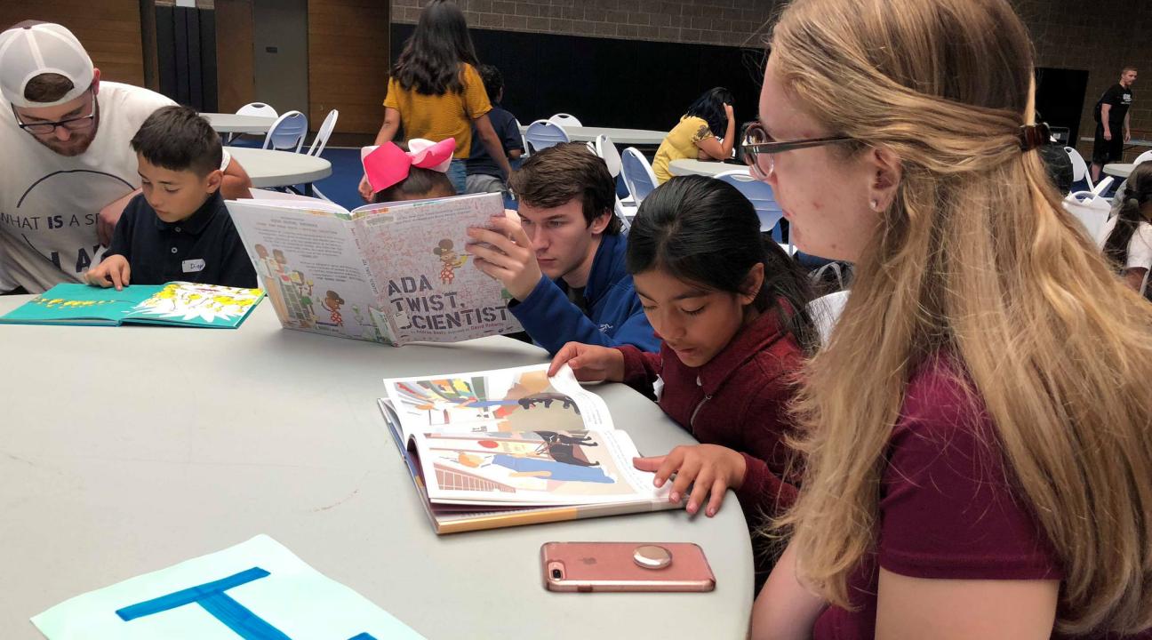 Elementary school students read to college students around a table